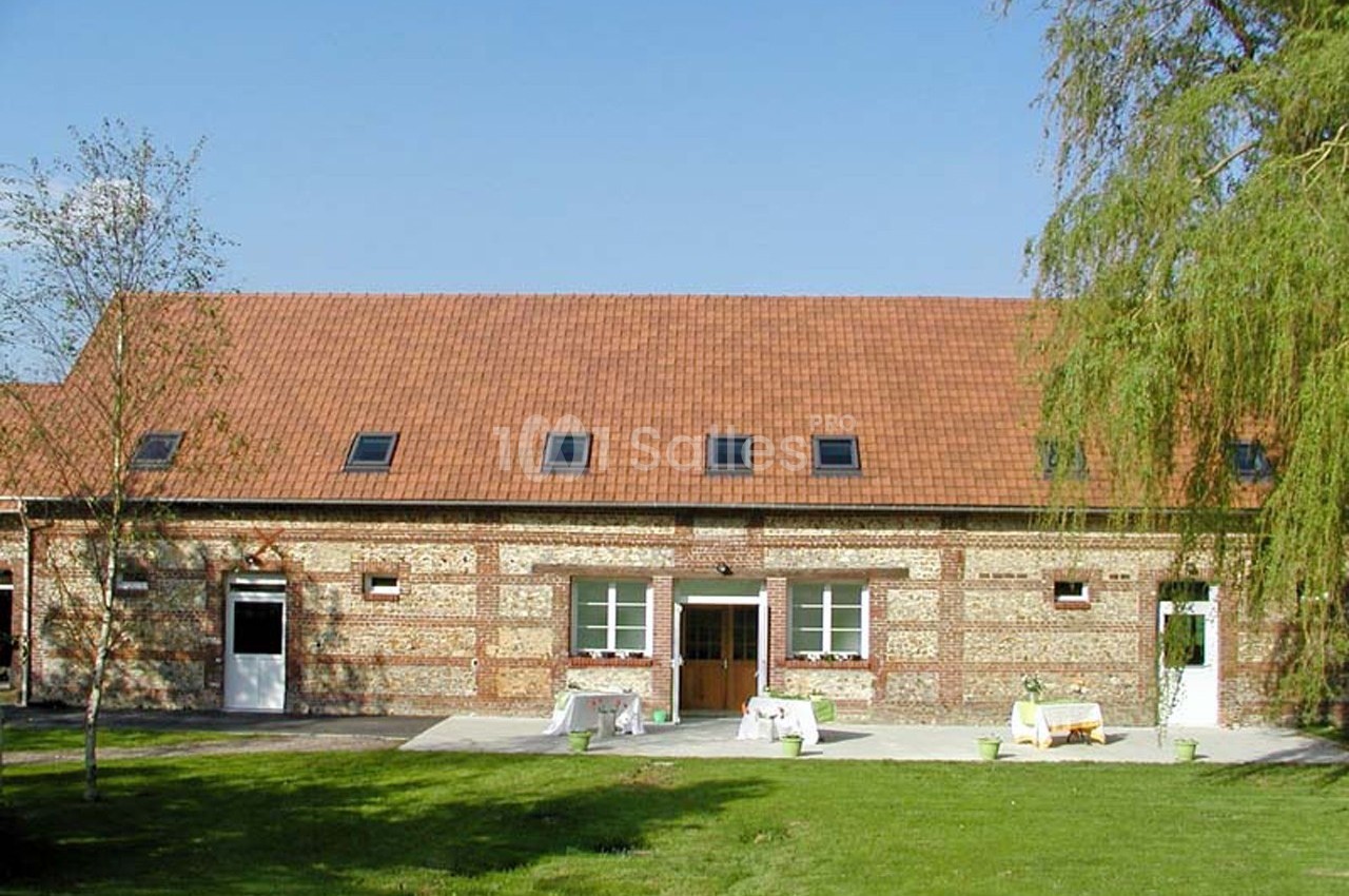 Bâtiment en briques avec toit en tuiles rouges, entouré d'une pelouse et d'arbres sous un ciel dégagé.