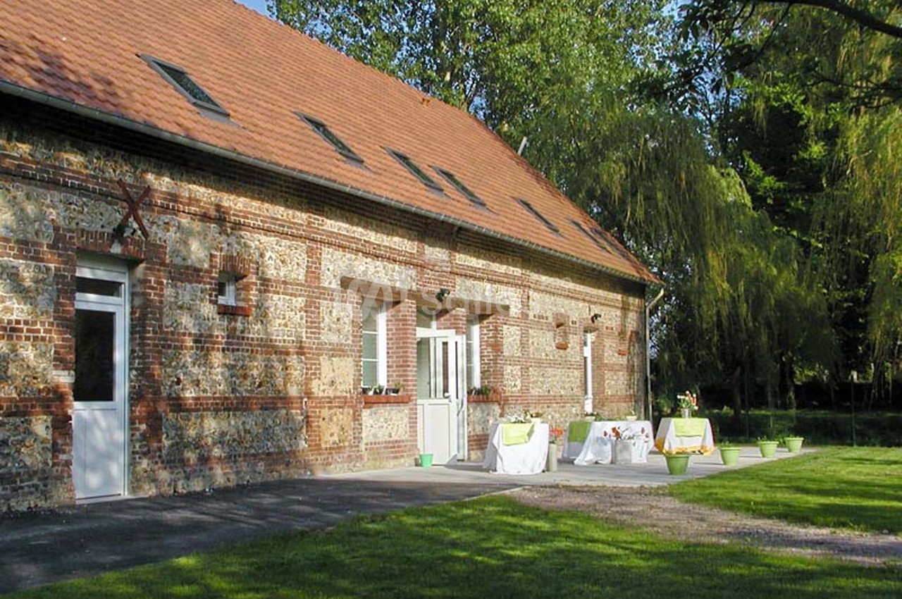 Façade en briques d'un bâtiment avec terrasse aménagée, tables dressées et jardin arboré en arrière-plan.