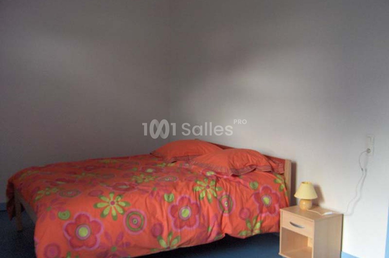 Lit double avec une housse de couette orange à motifs floraux, table de chevet en bois avec lampe dans une chambre sobre.