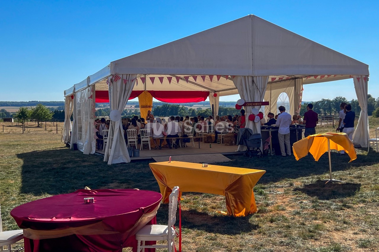 Tente blanche ouverte accueillant un événement avec des invités assis, décorations colorées et tables en extérieur.
