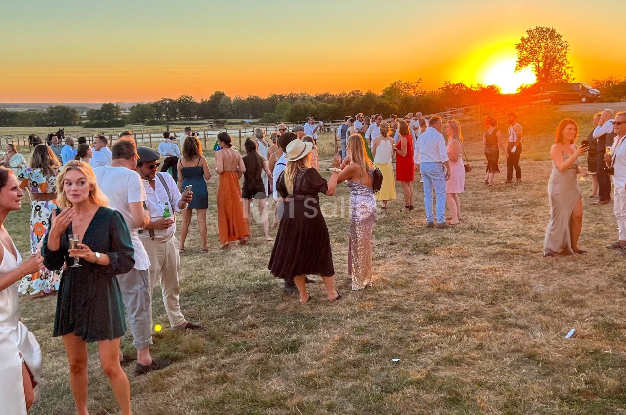 Groupe de personnes discutant en plein air lors d'un événement au coucher du soleil, dans un cadre champêtre.