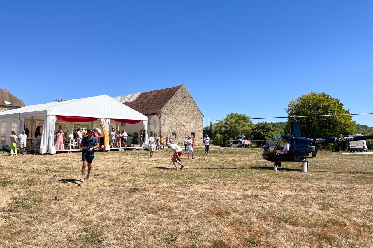 Un hélicoptère posé sur un terrain herbeux près d'une tente blanche où des personnes sont rassemblées.