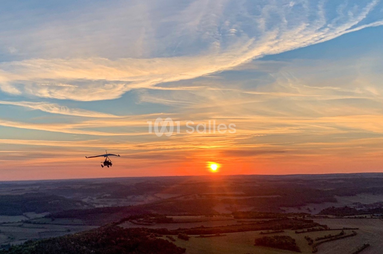 Un autogire volant au-dessus d'un paysage vallonné au coucher du soleil avec un ciel aux teintes orangées et bleues.