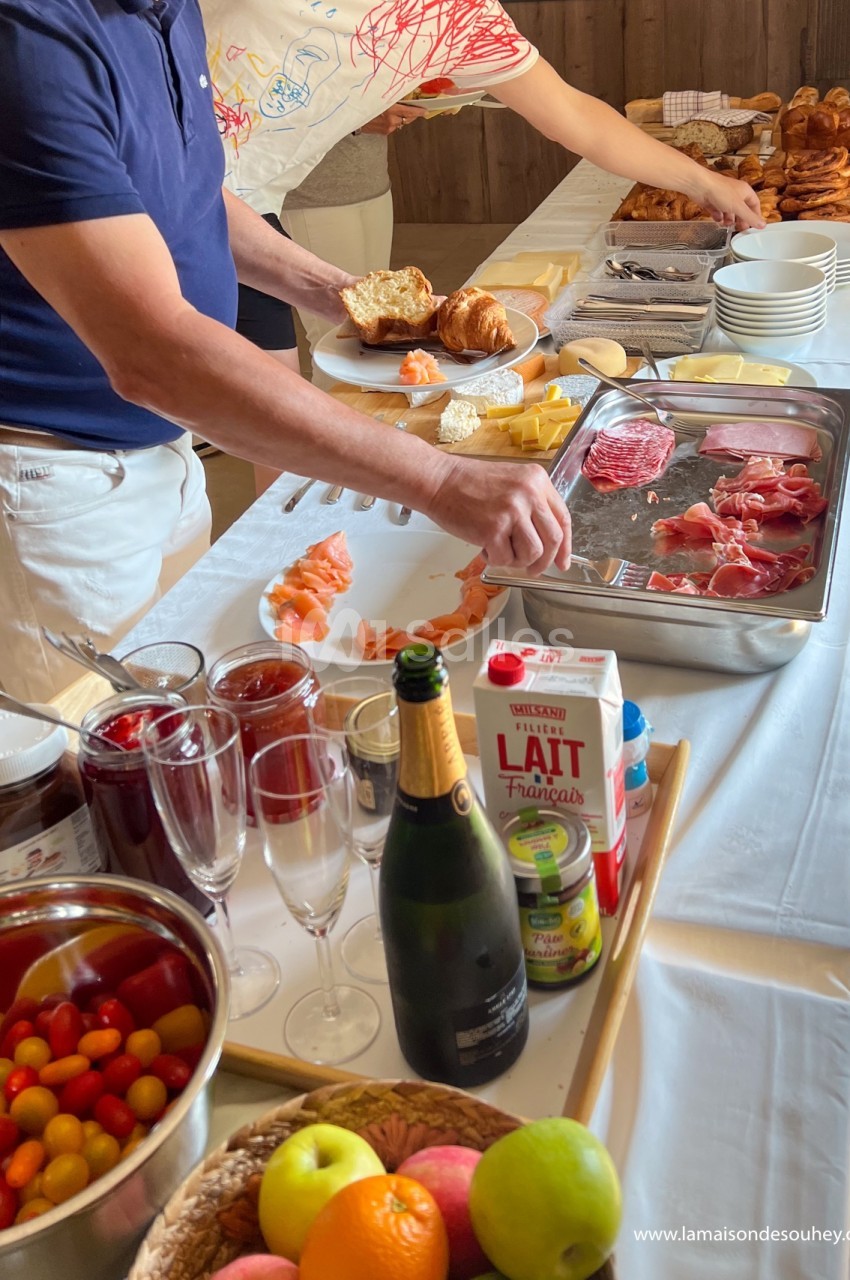 Buffet de petit-déjeuner avec viennoiseries, charcuterie, fromages, fruits, jus et boissons disposés sur une table.