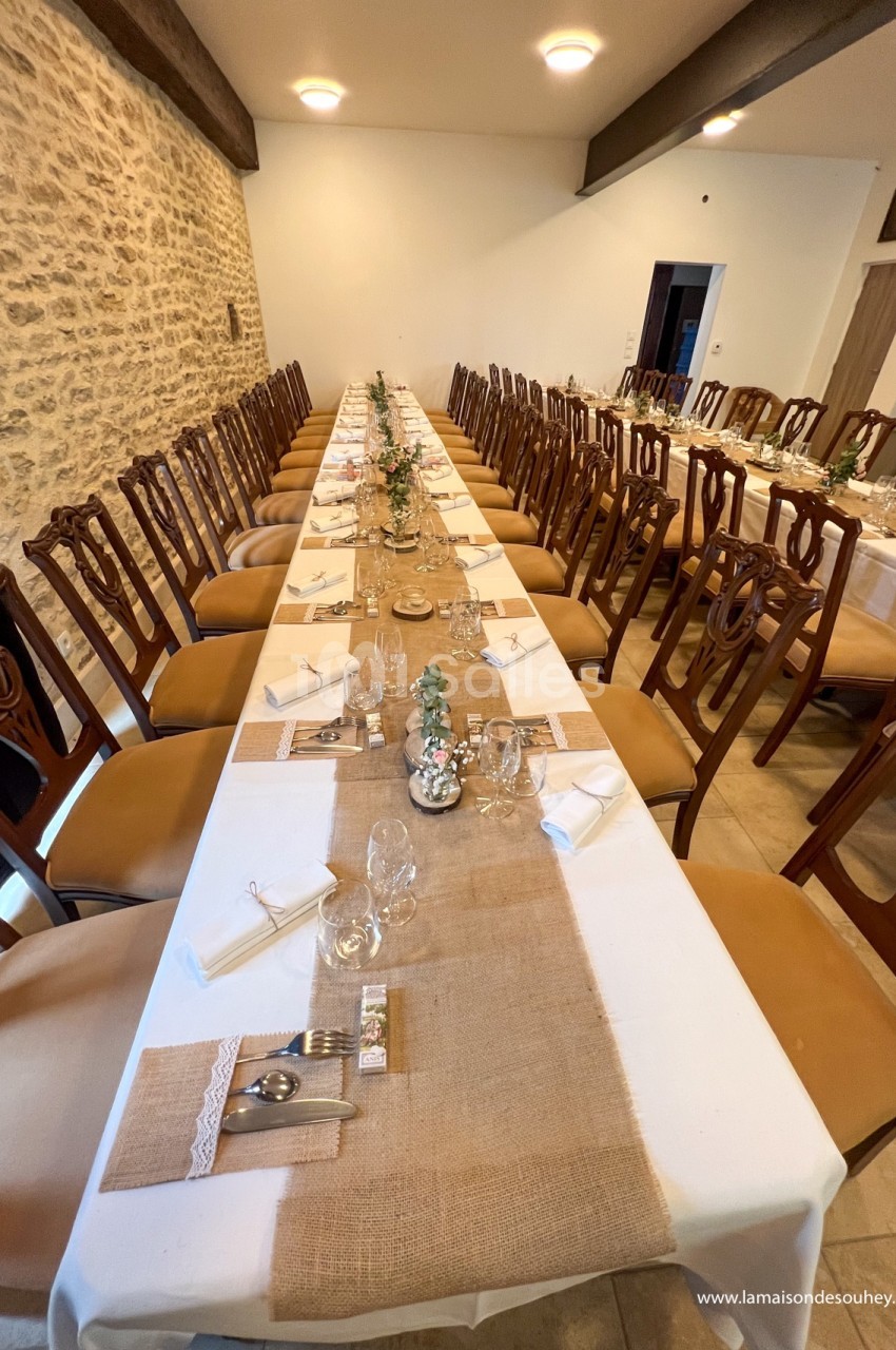 Grande table de banquet décorée avec des chemins de table en toile de jute, vaisselle élégante et chaises en bois.