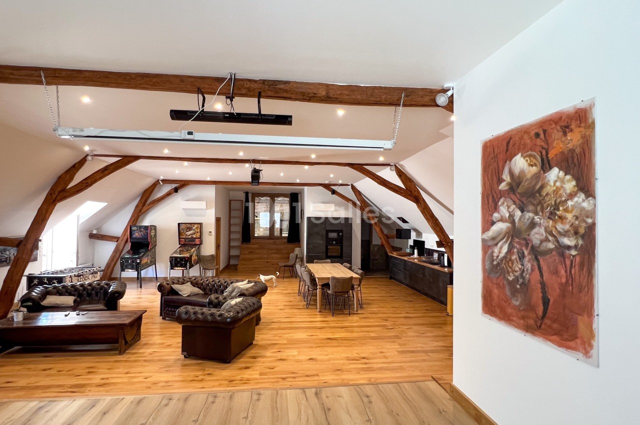 Espace de vie lumineux avec poutres apparentes, mobilier en bois et coin salon, salle à manger et cuisine ouverte.
