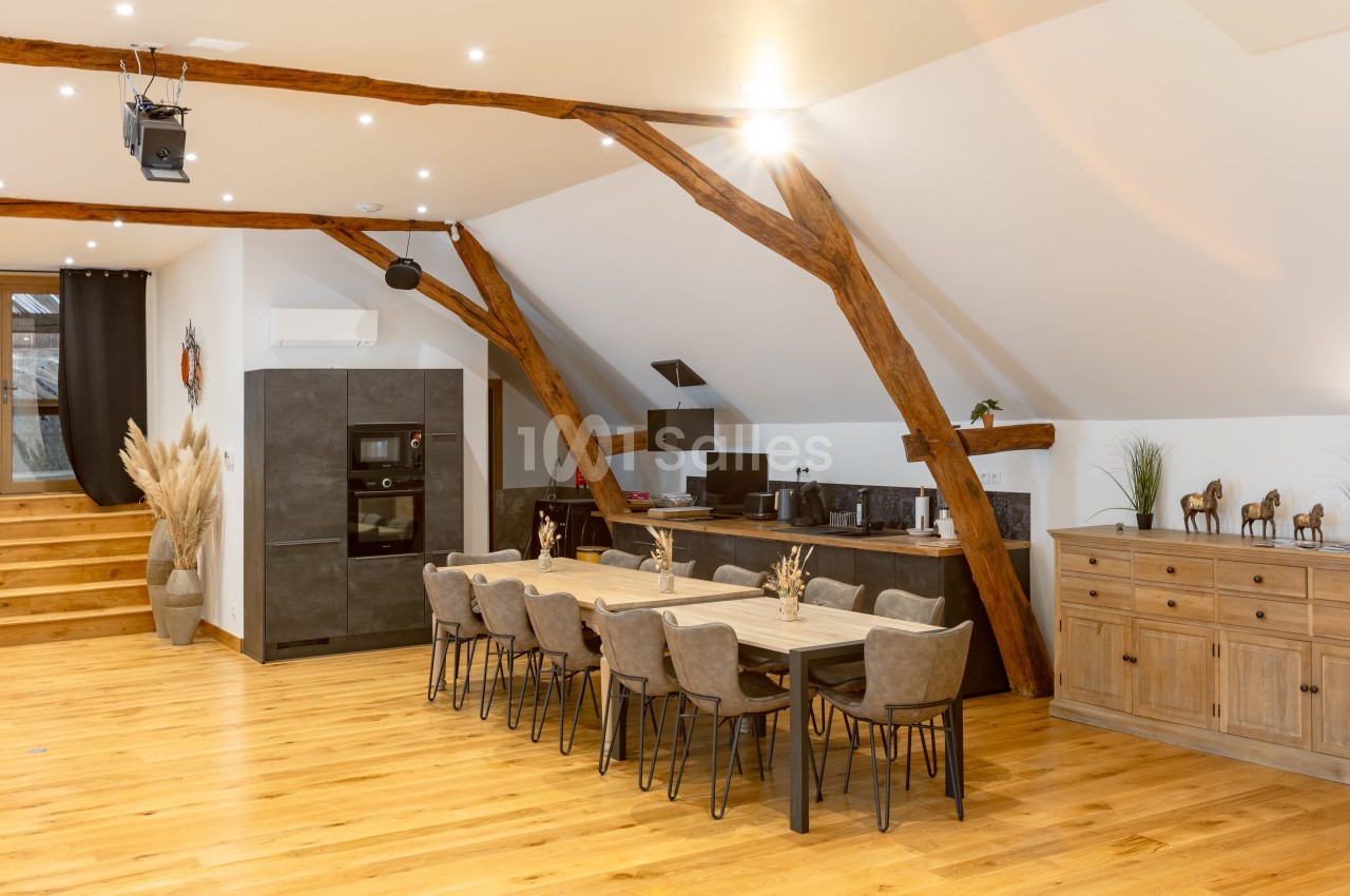 Salle à manger spacieuse avec table en bois, chaises modernes, cuisine ouverte et poutres apparentes sous un plafond…