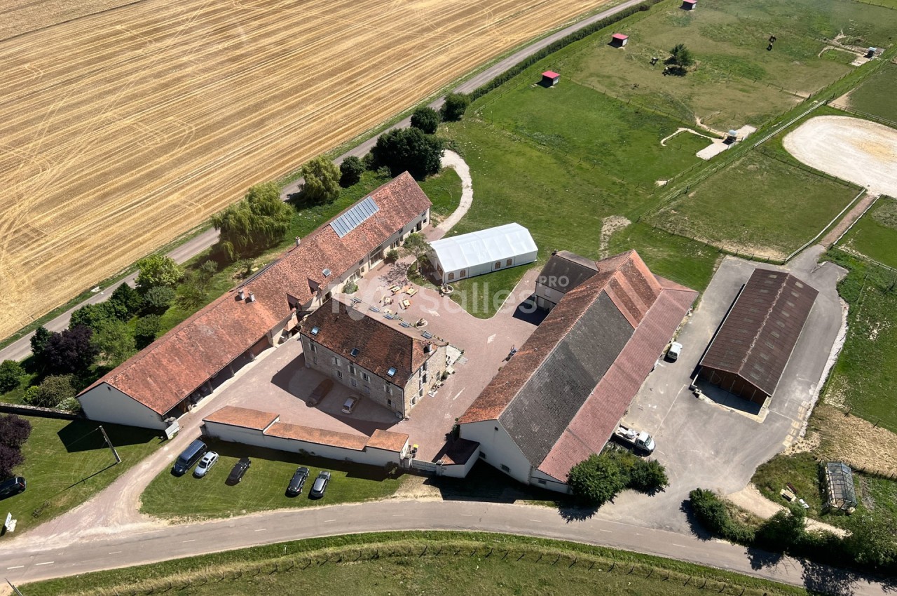 Vue aérienne d'un domaine rural avec bâtiments en U, cours centrale, champs et espaces verts environnants.