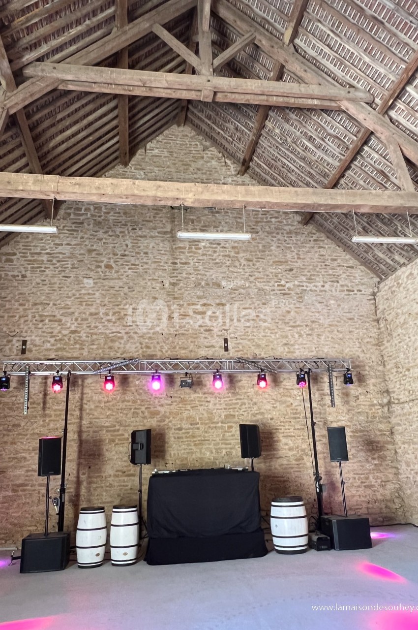 Salle en pierre avec charpente apparente, équipée d'un système de sonorisation et d'éclairage coloré.