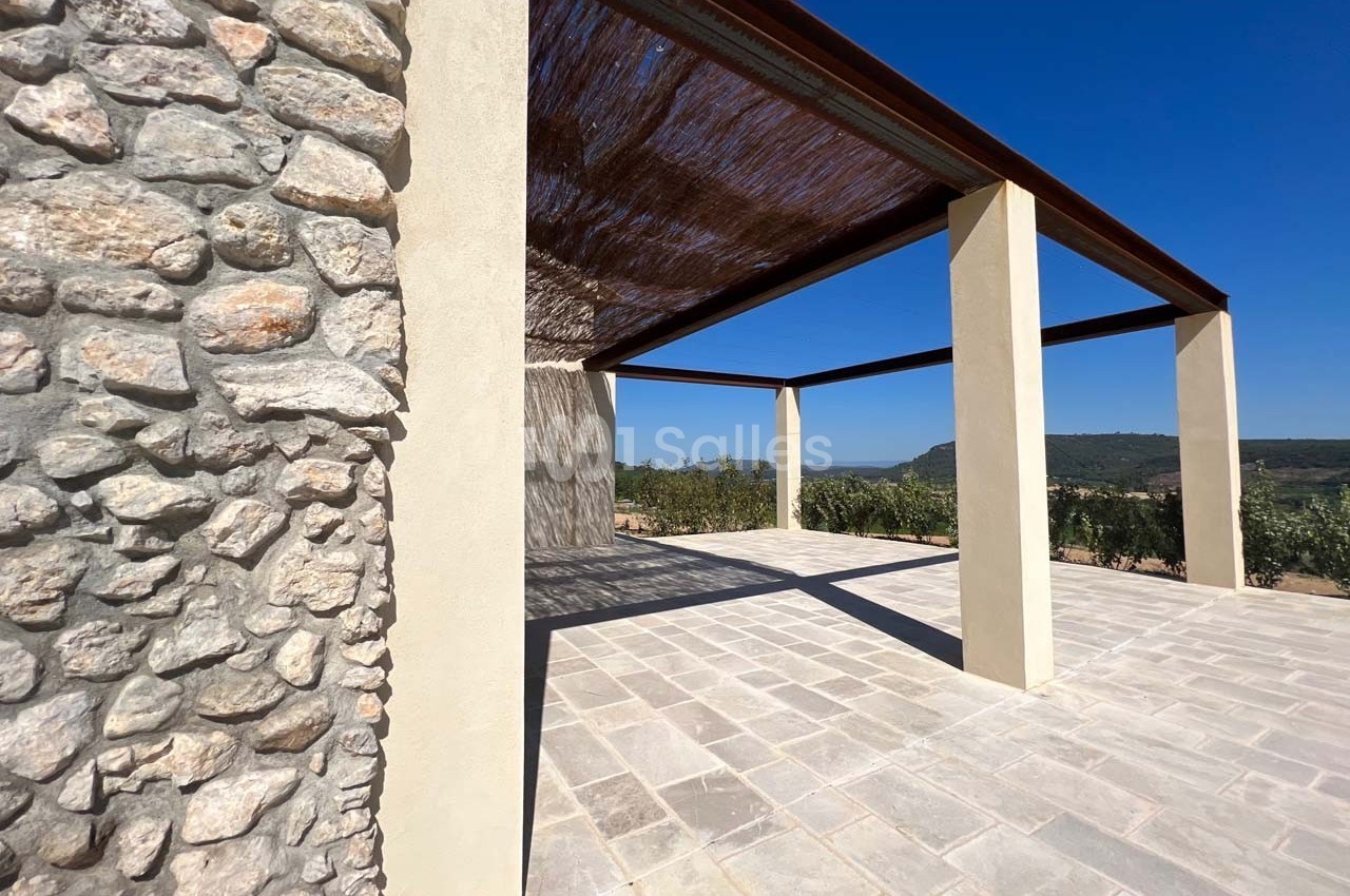 Structure en pierre et piliers modernes soutenant une pergola avec vue dégagée sur un paysage naturel ensoleillé.