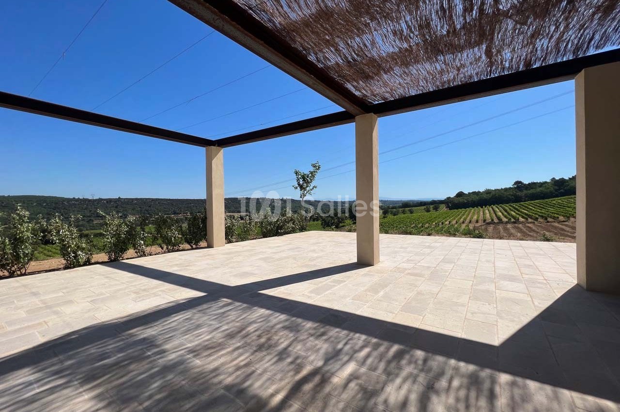 Terrasse ombragée avec vue sur des vignes et collines sous un ciel bleu dégagé.