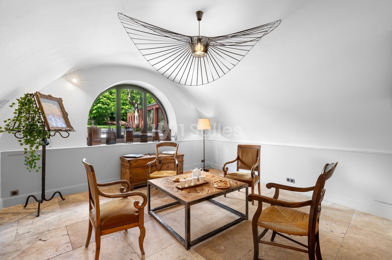 Salle lumineuse avec table basse en bois, quatre chaises, une lampe design et une grande fenêtre en arche donnant sur un…