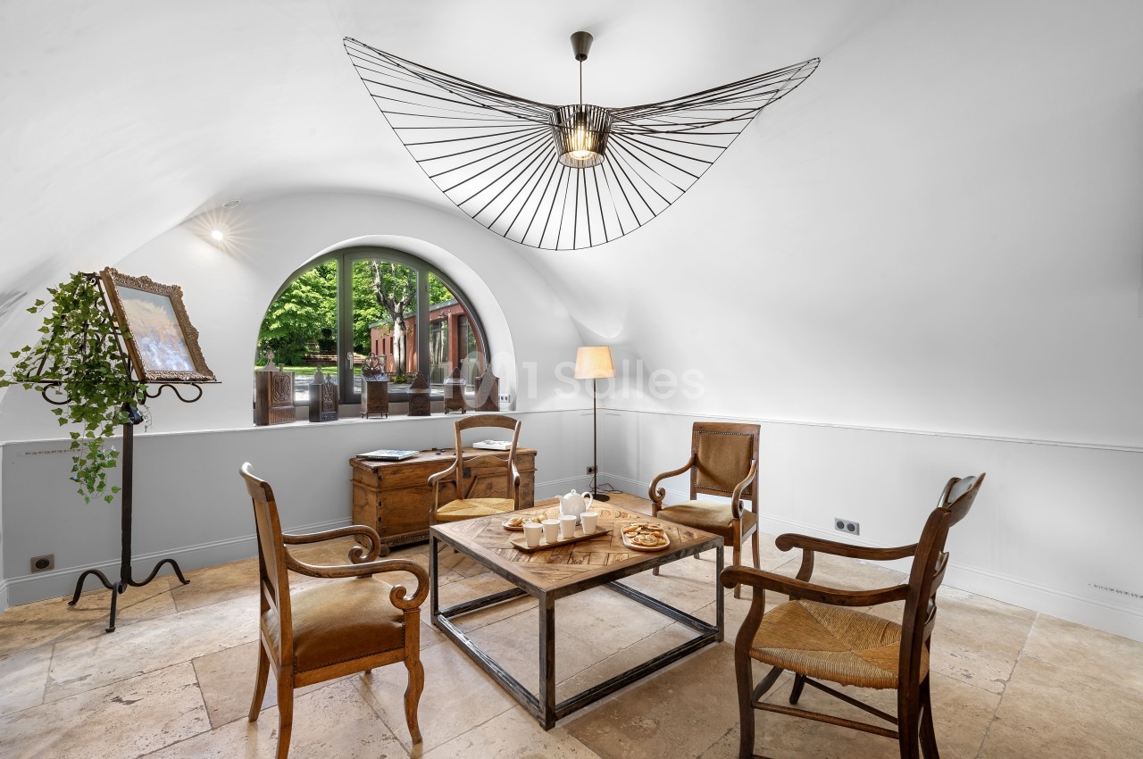 Salle lumineuse avec quatre chaises en bois autour d'une table basse, grande fenêtre cintrée et décoration minimaliste.