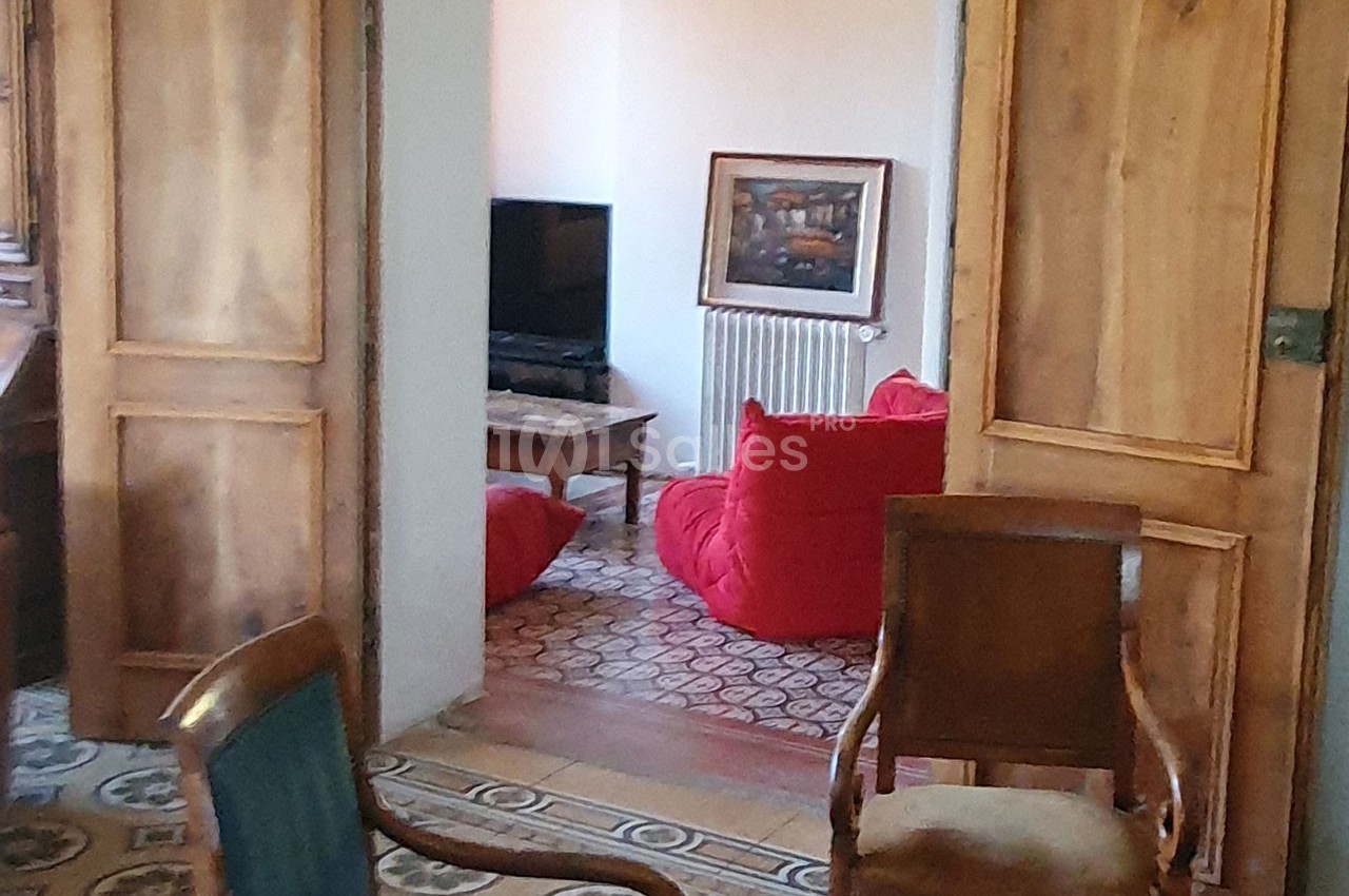 Une pièce avec des fauteuils, une télévision, un tapis à motifs et des portes en bois ouvertes.