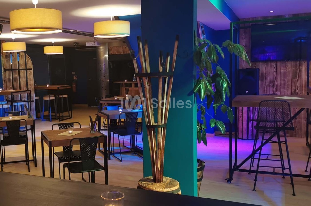 Salle de restaurant moderne avec tables en bois, chaises noires, éclairage chaleureux et décoration végétale.