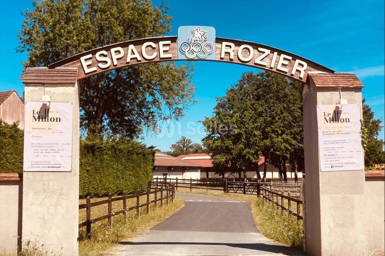 Entrée de l'Espace Rozier avec une arche en pierre, des panneaux d'information et un chemin menant à des bâtiments.