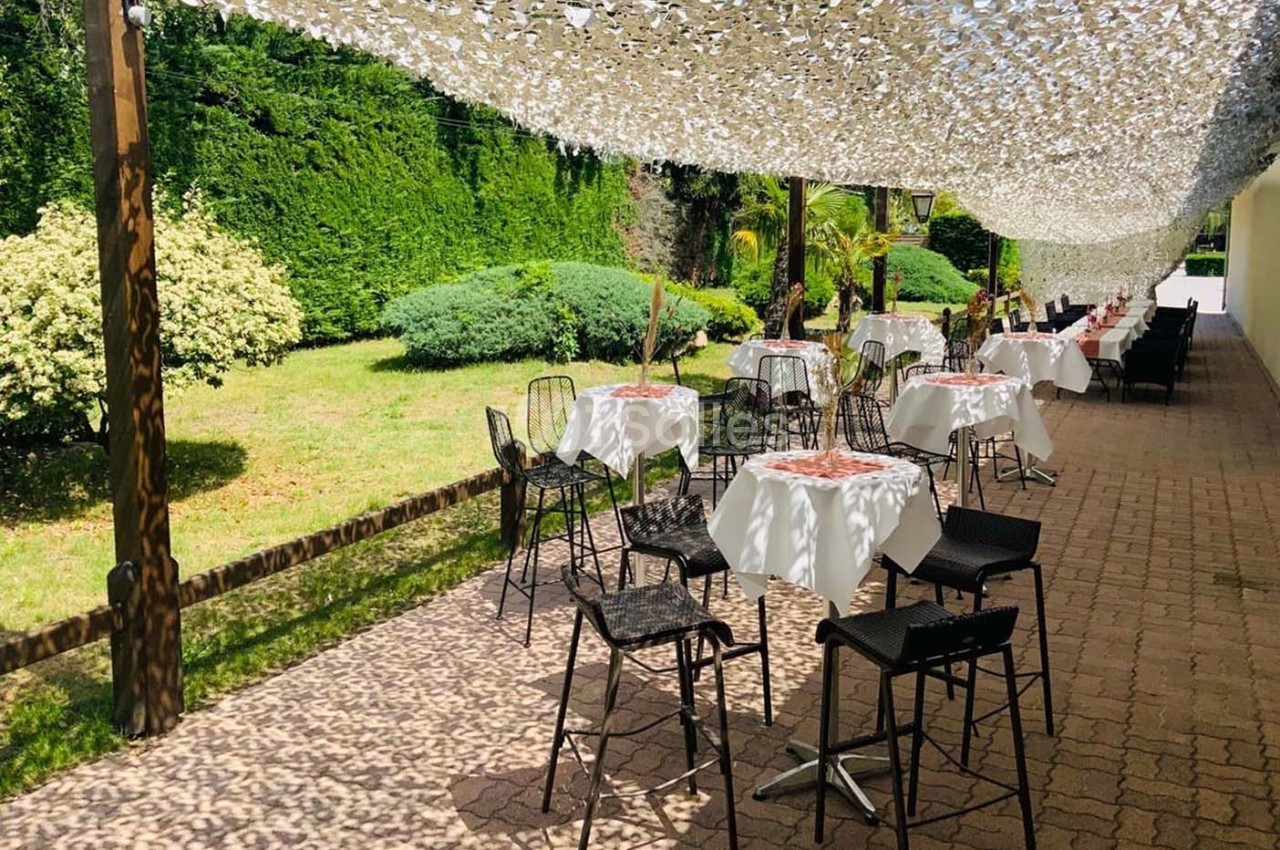 Terrasse ombragée avec tables et chaises disposées près d'un jardin verdoyant.
