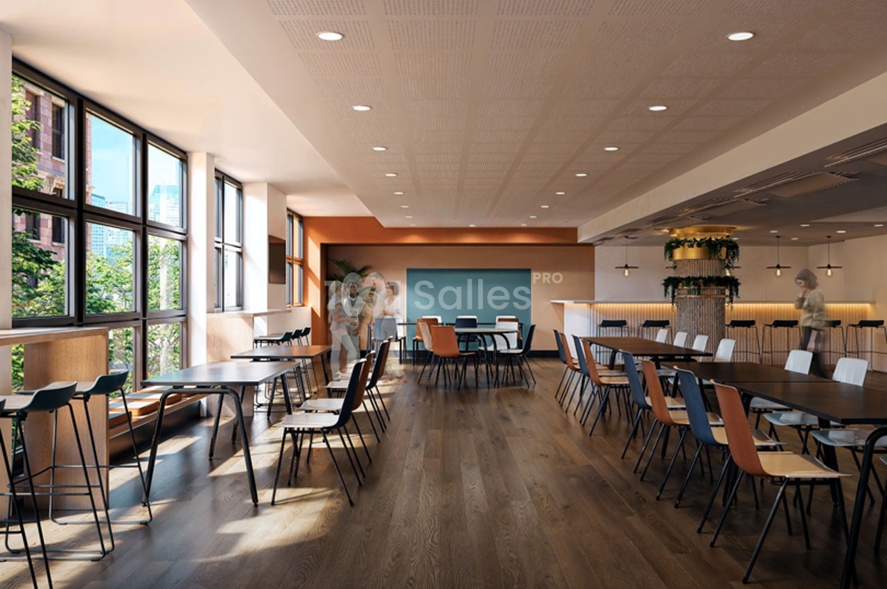 Salle lumineuse avec de grandes fenêtres, tables en bois, chaises colorées et décoration végétale.