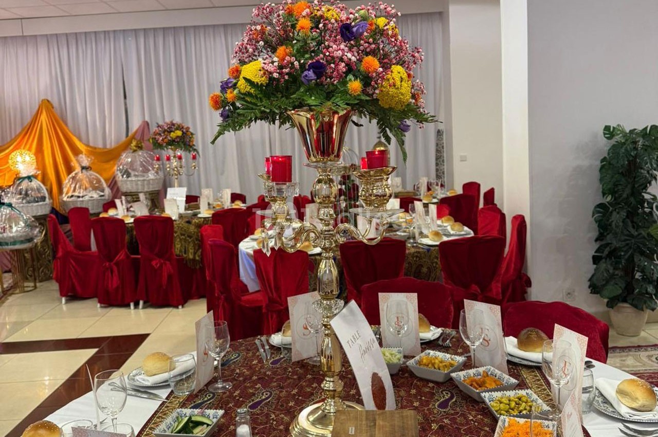 Table décorée pour un événement avec nappes rouges, chandelier doré orné de fleurs colorées et plats disposés.
