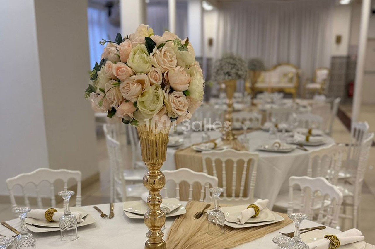 Salle de réception élégante avec tables dressées, décorations florales et chaises blanches.