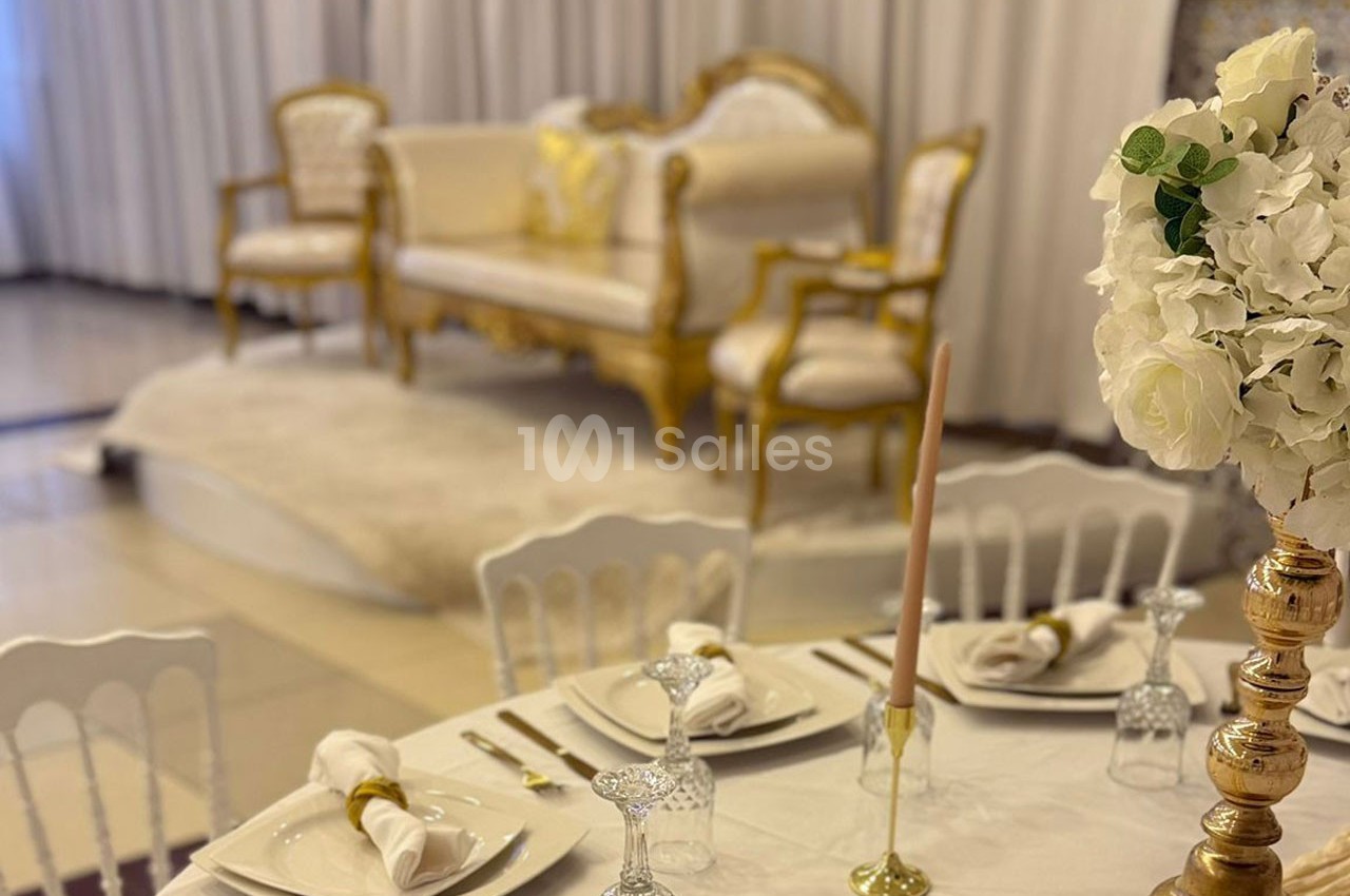 Salle décorée avec un canapé doré, des chaises assorties et une table dressée avec vaisselle élégante et bougies.