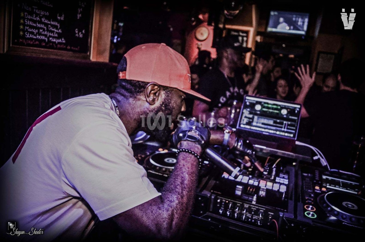 Un DJ mixant sur des platines dans un club animé avec des écrans et un public en arrière-plan.