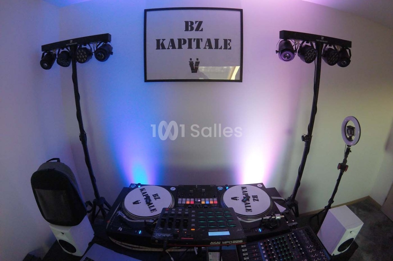 Deux platines, une table de mixage et des éclairages installés dans une pièce avec un cadre ’BZ KAPITALE’ au mur.
