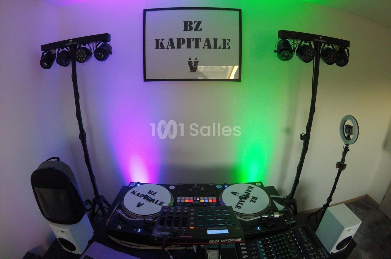 Équipement de DJ avec platines, table de mixage et éclairages colorés dans une pièce décorée sobrement.