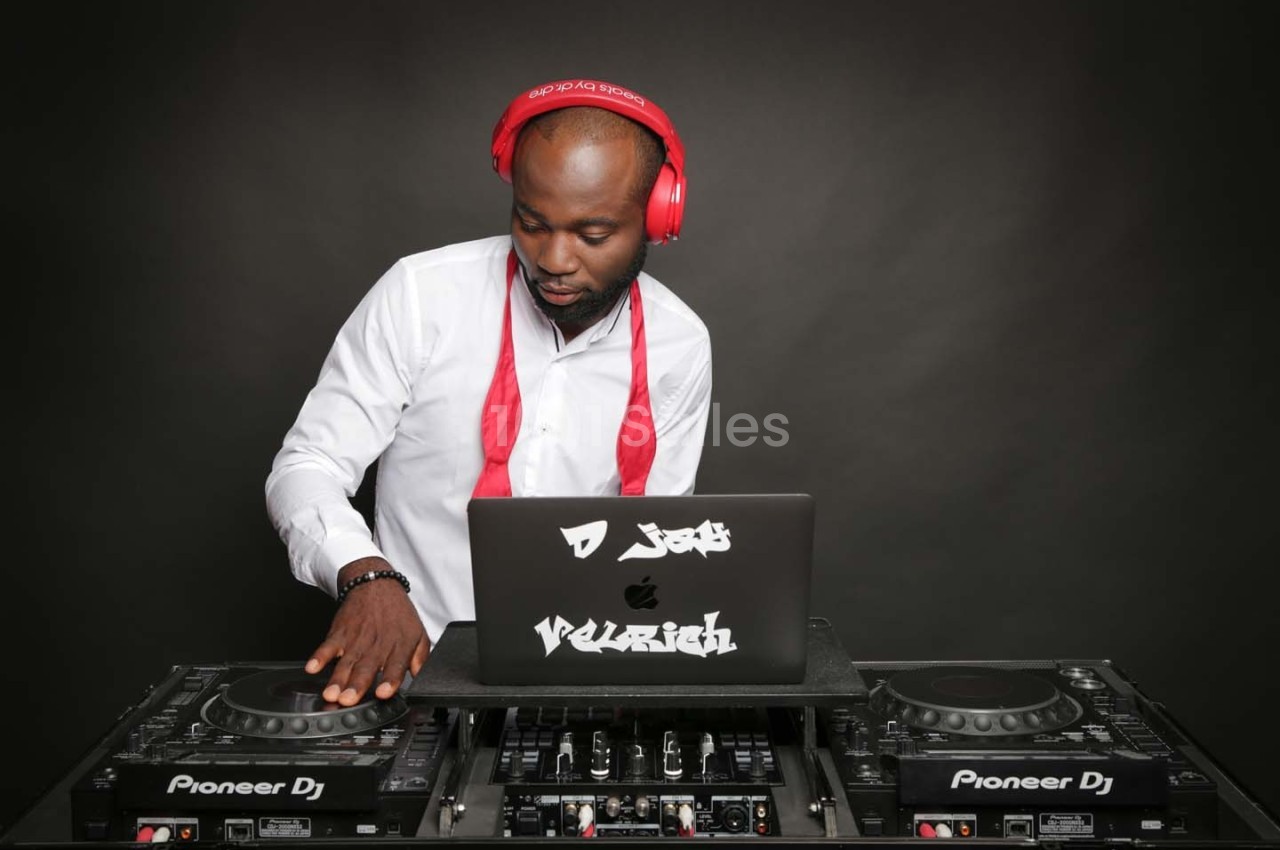 Un DJ portant un casque rouge mixe de la musique sur une table de mixage avec un ordinateur portable.