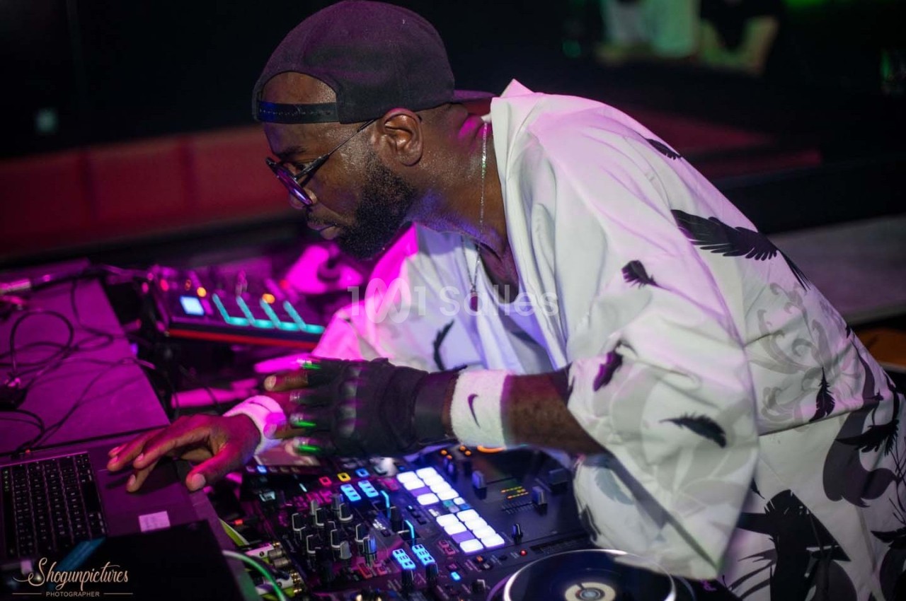 Un DJ mixant sur une table de mixage dans un environnement sombre avec des lumières colorées.