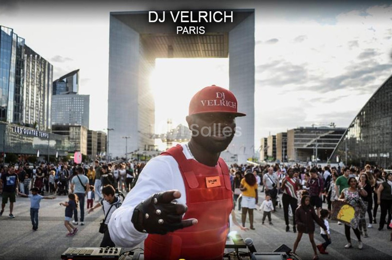 Un DJ mixe en plein air devant une foule, avec l'Arche de la Défense en arrière-plan.
