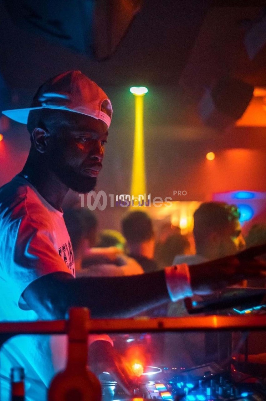 Un DJ mixant sur une console dans une ambiance de boîte de nuit avec éclairages colorés.