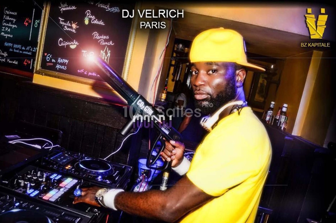 Un DJ en tenue jaune mixant de la musique dans un club avec des platines et un micro à la main.