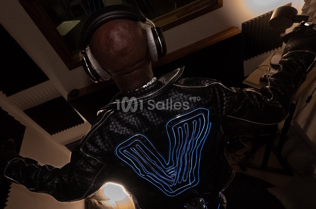 Personne de dos portant un casque audio et une veste avec un motif lumineux, dans un studio d'enregistrement.