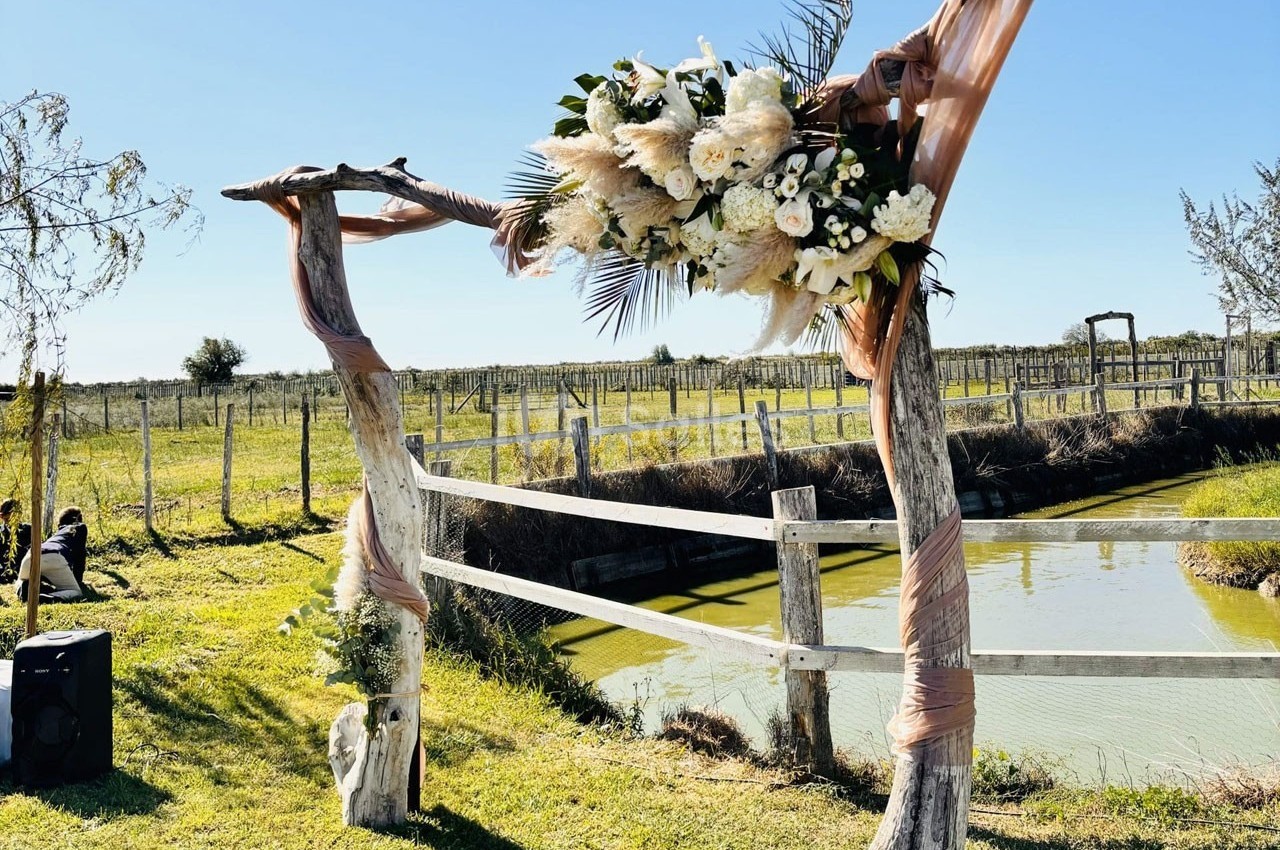 Arche en bois décorée de fleurs blanches et feuillages, installée près d'un étang dans un cadre champêtre.