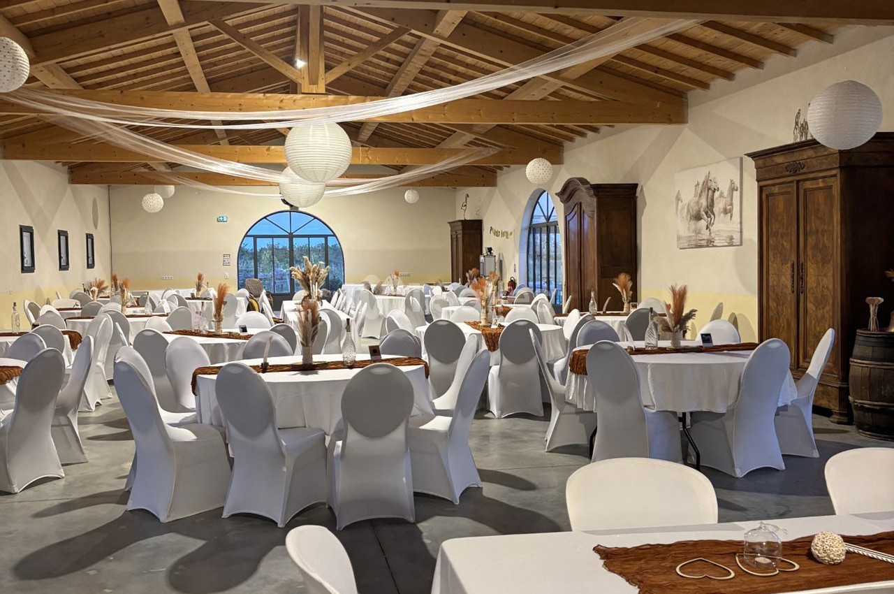 Salle de réception décorée avec des tables rondes et rectangulaires, nappes blanches et éléments rustiques.