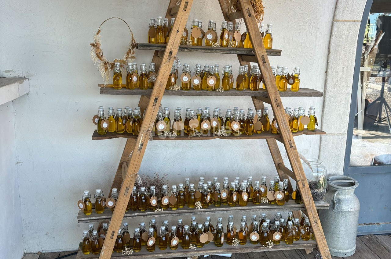 Étagère en bois en forme de triangle exposant des bouteilles d'huile disposées en rangées sur plusieurs niveaux.