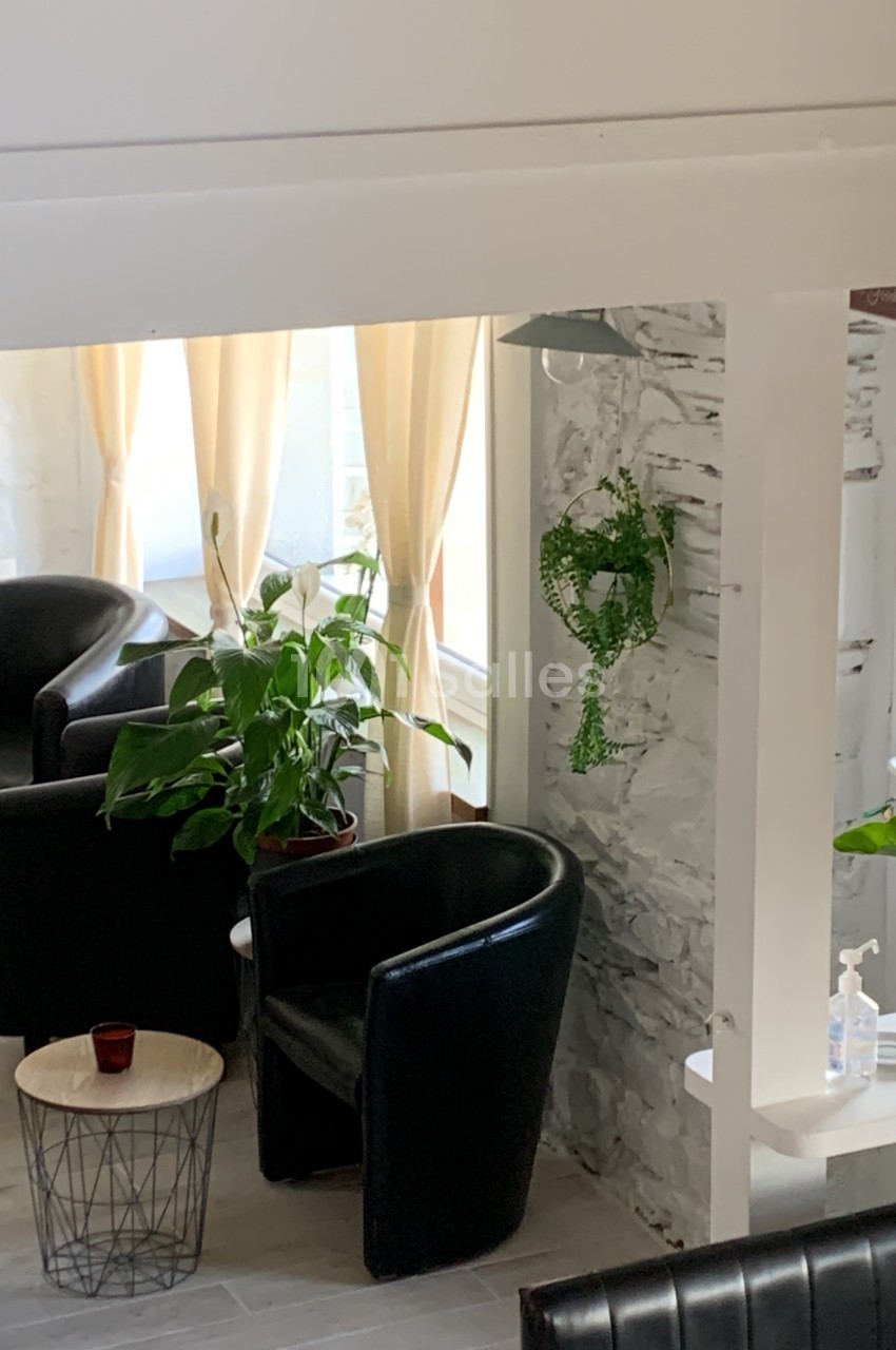 Deux fauteuils noirs près d'une table basse, entourés de plantes et éclairés par une lumière naturelle.