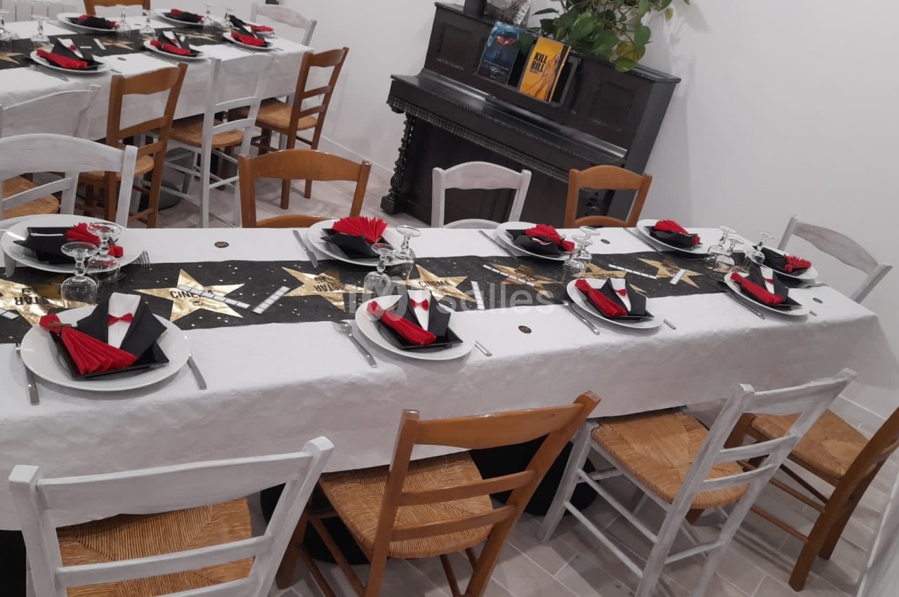 Table dressée avec une nappe blanche, décorée de motifs étoilés noirs et dorés, avec serviettes rouges et noires.