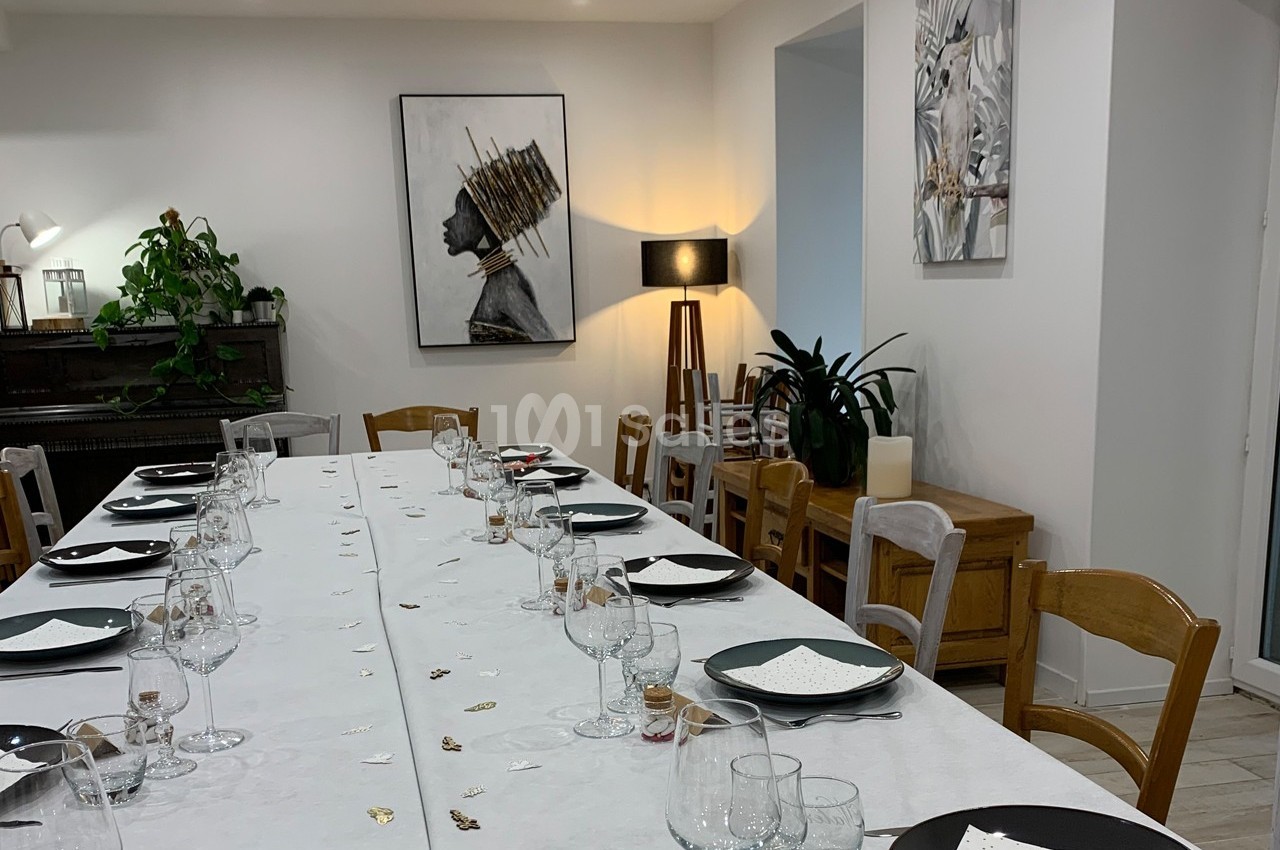 Table dressée avec vaisselle et décorations dans une salle lumineuse, ornée de plantes et de tableaux modernes.