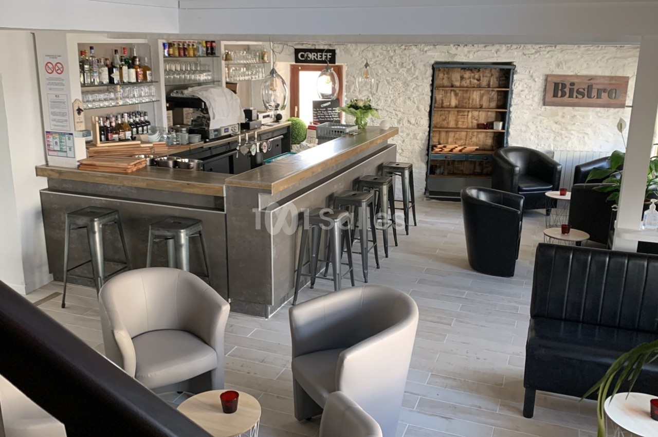 Intérieur d'un bar moderne avec comptoir, tabourets hauts, fauteuils, et décoration murale en pierre apparente.