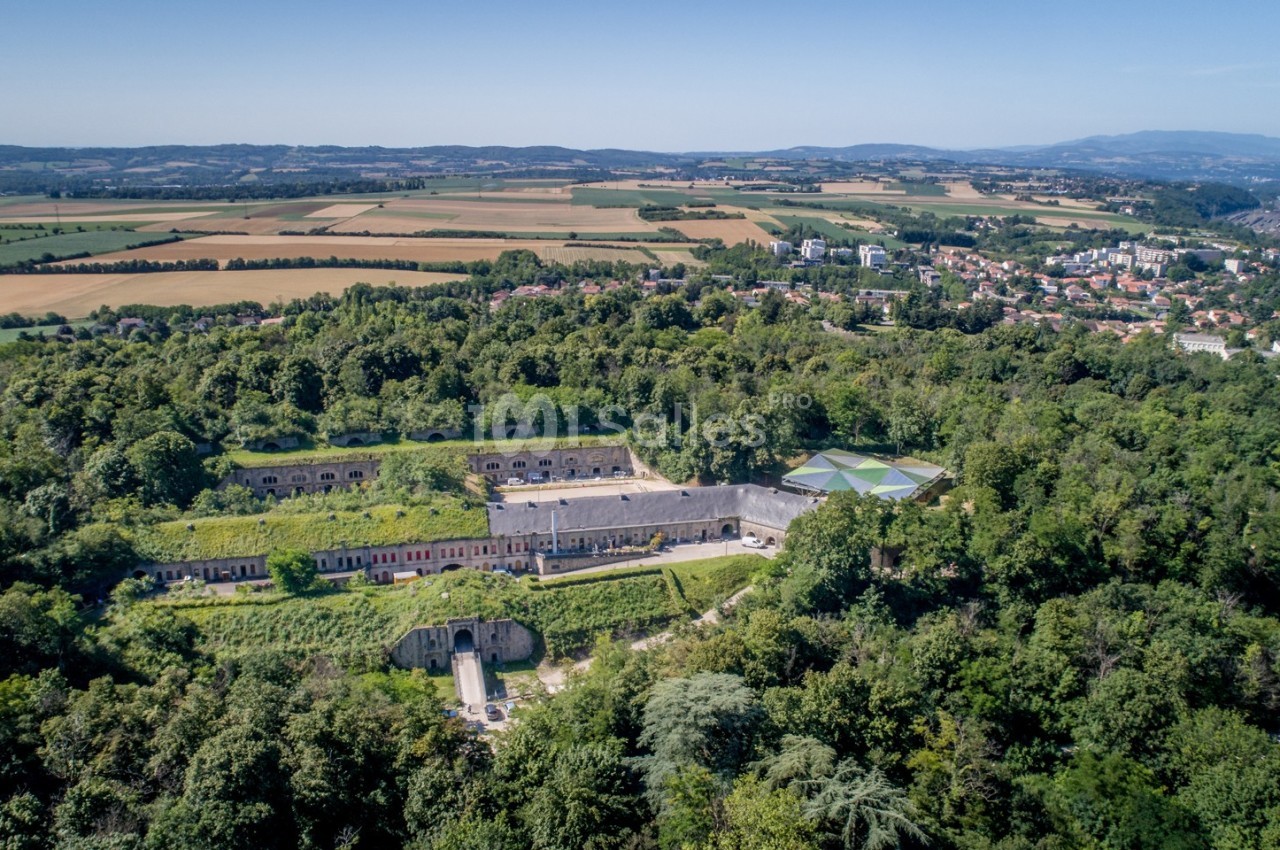 Vue aérienne d'un fort entouré de végétation, avec des champs et une ville en arrière-plan.
