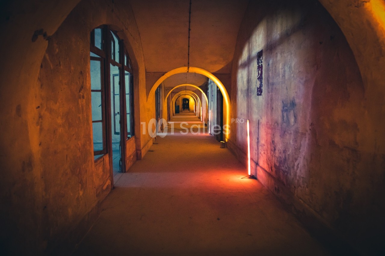 Couloir ancien avec arches éclairé par des lumières colorées, créant une ambiance chaleureuse et mystérieuse.