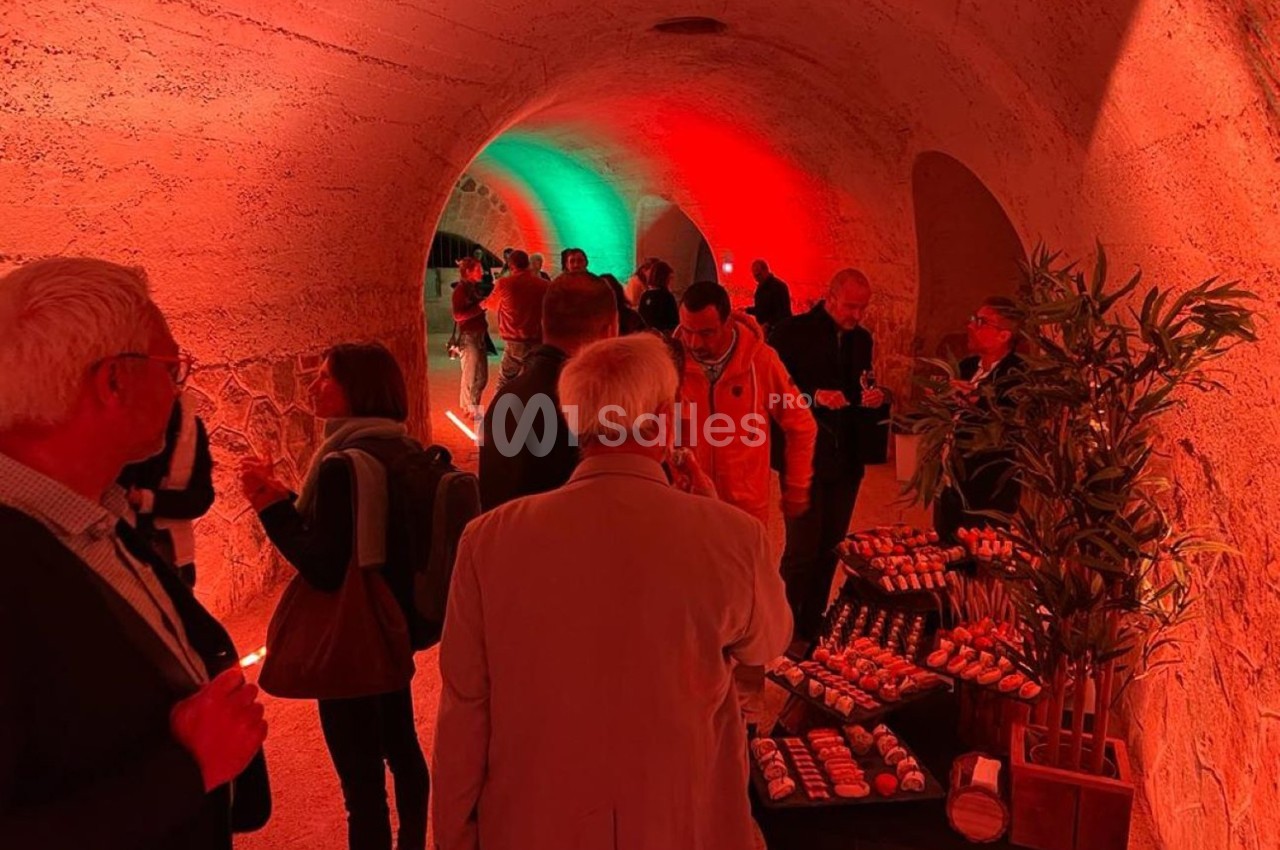 Des personnes discutent dans un tunnel éclairé en rouge et vert, avec une table de petits fours au premier plan.