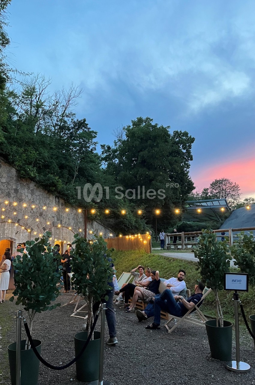 Personnes assises sur des chaises longues dans un espace extérieur éclairé par des guirlandes, au coucher du soleil.