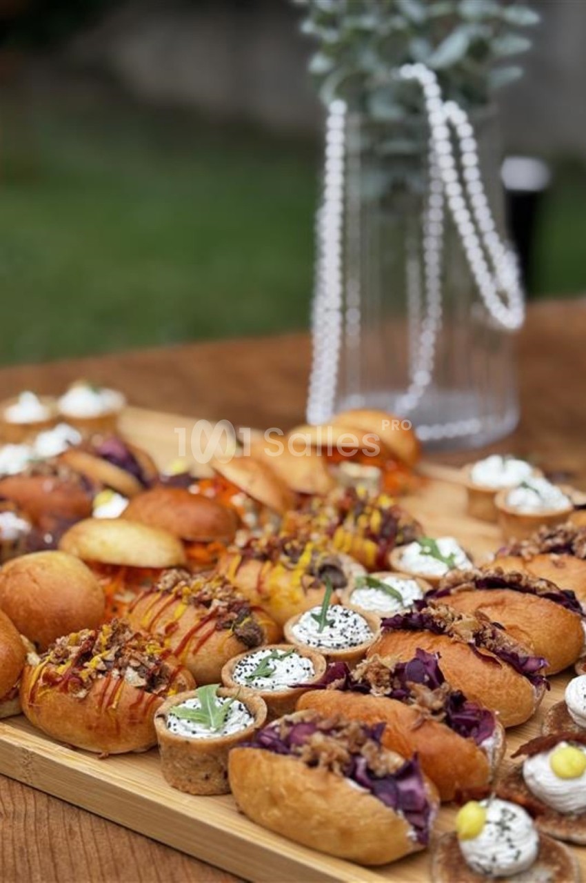 Plateau en bois garni de mini-sandwichs variés, bouchées apéritives et verrines, posé sur une table en extérieur.