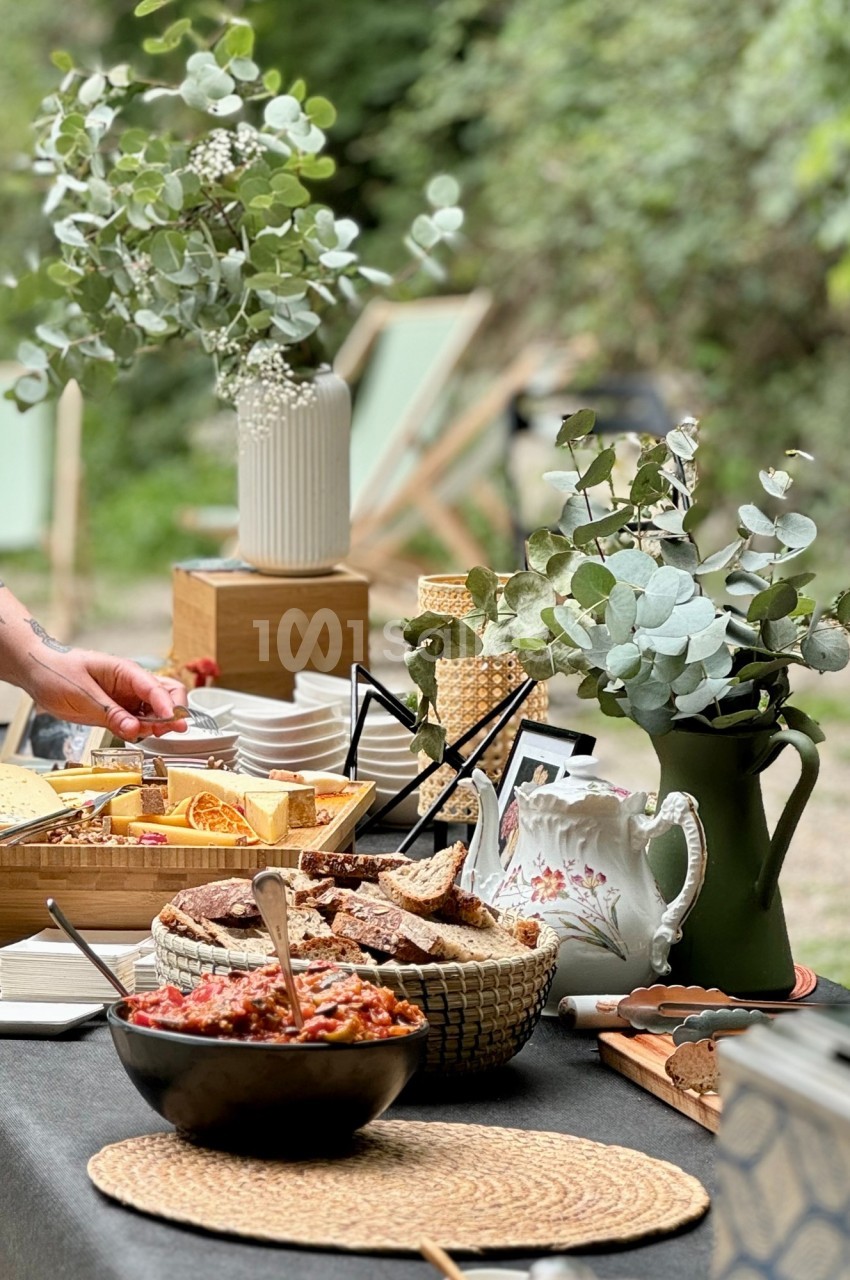 Buffet en plein air avec des plats variés, des fleurs en vase et une ambiance naturelle entourée de verdure.