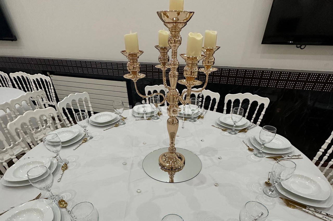Table ronde dressée avec une nappe blanche, couverts, verres et un chandelier doré au centre avec des bougies.