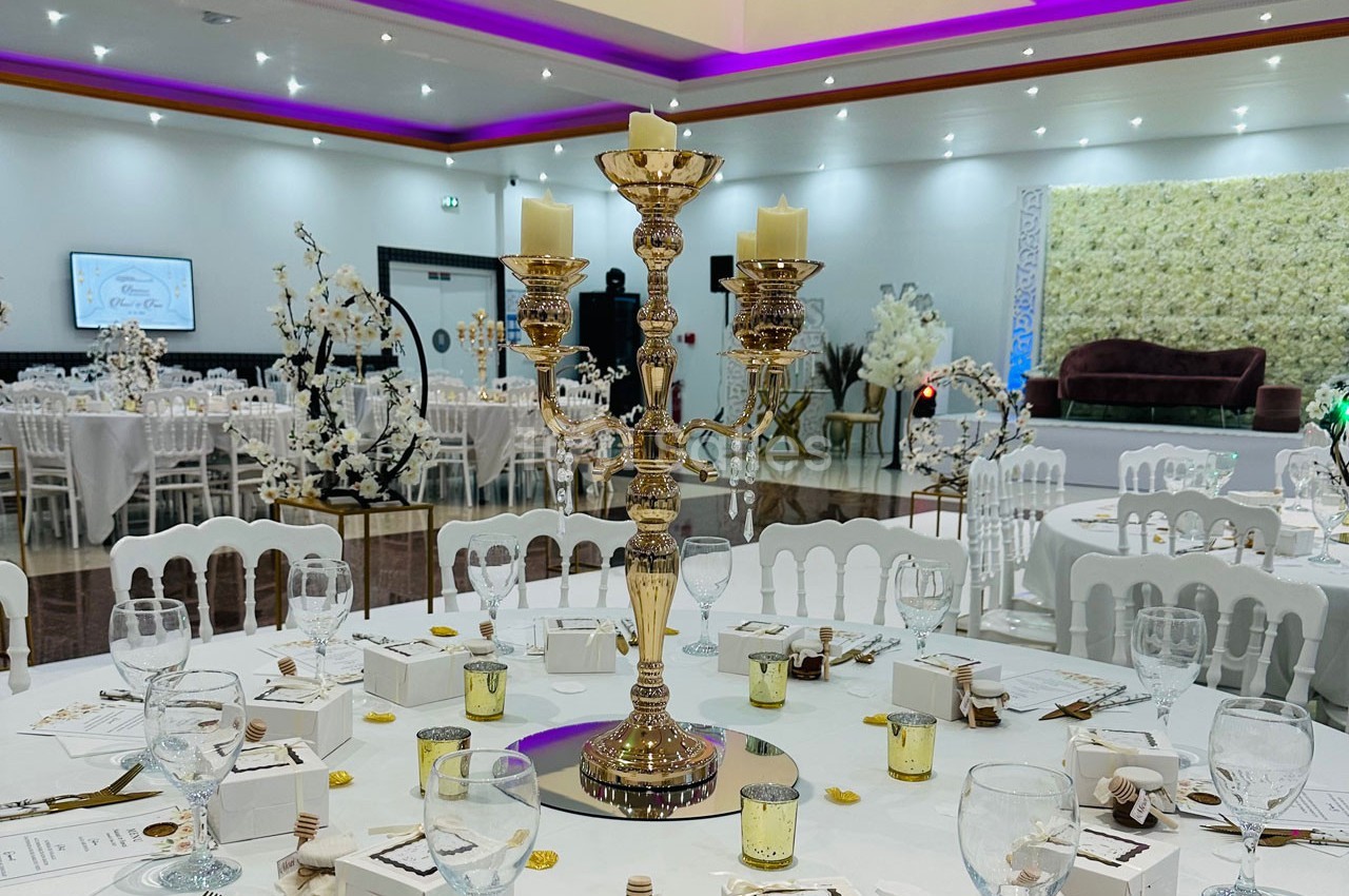 Salle de réception décorée avec des tables rondes, un chandelier doré central et des lumières d'ambiance violettes.