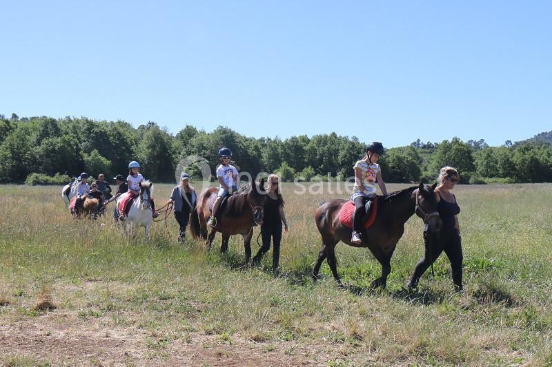 Un groupe d'enfants et d'adultes monte à cheval dans un champ sous un ciel dégagé.